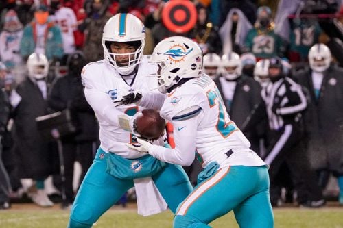 Jan 13, 2024; Kansas City, Missouri, USA; Miami Dolphins quarterback Tua Tagovailoa (1) hands off to running back De'Von Achane (28) against the Kansas City Chiefs in a 2024 AFC wild card game at GEHA Field at Arrowhead Stadium.