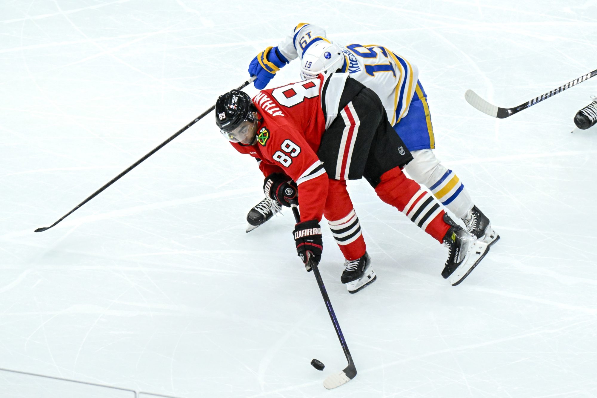 Oct 19, 2024; Chicago, Illinois, USA; Chicago Blackhawks center Andreas Athanasiou (89) fights for the puck with Buffalo Sabres center Peyton Krebs (19) during the third period at the United Center.